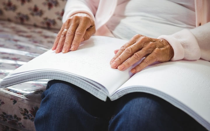 Frau liest doppelseitigen Druck von Blindenschrift